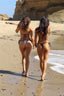 Two women in bikinis walking on a beach 