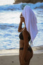 A person standing at the beach wearing a black bikini bottom with a towel draped over their head.